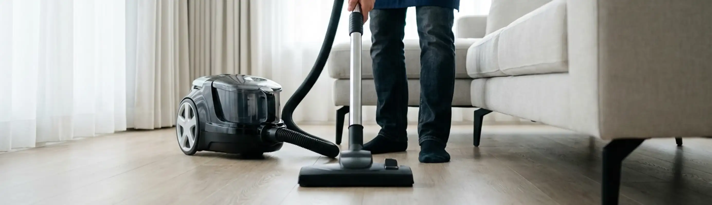 Professional house cleaner vacuuming a living room floor with a canister vacuum cleaner, San Antonio, TX.