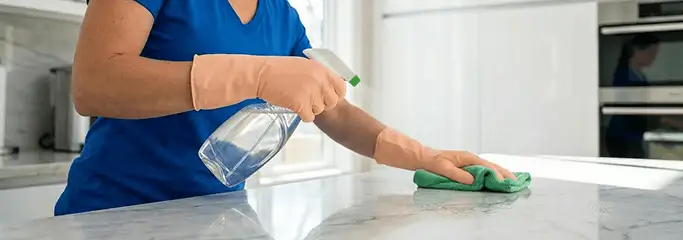 Maid service worker spraying and wiping a kitchen countertop with a microfiber cloth for sanitizing, San Antonio, TX.