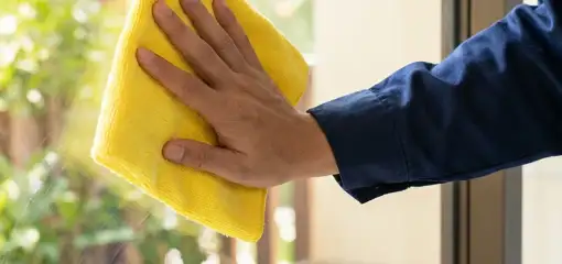 House cleaner wiping a glass window with a yellow microfiber cloth for streak-free cleaning, San Antonio, TX.
